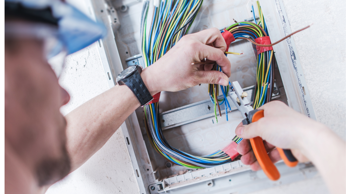 A man is working on an electrical box with a pair of pliers.