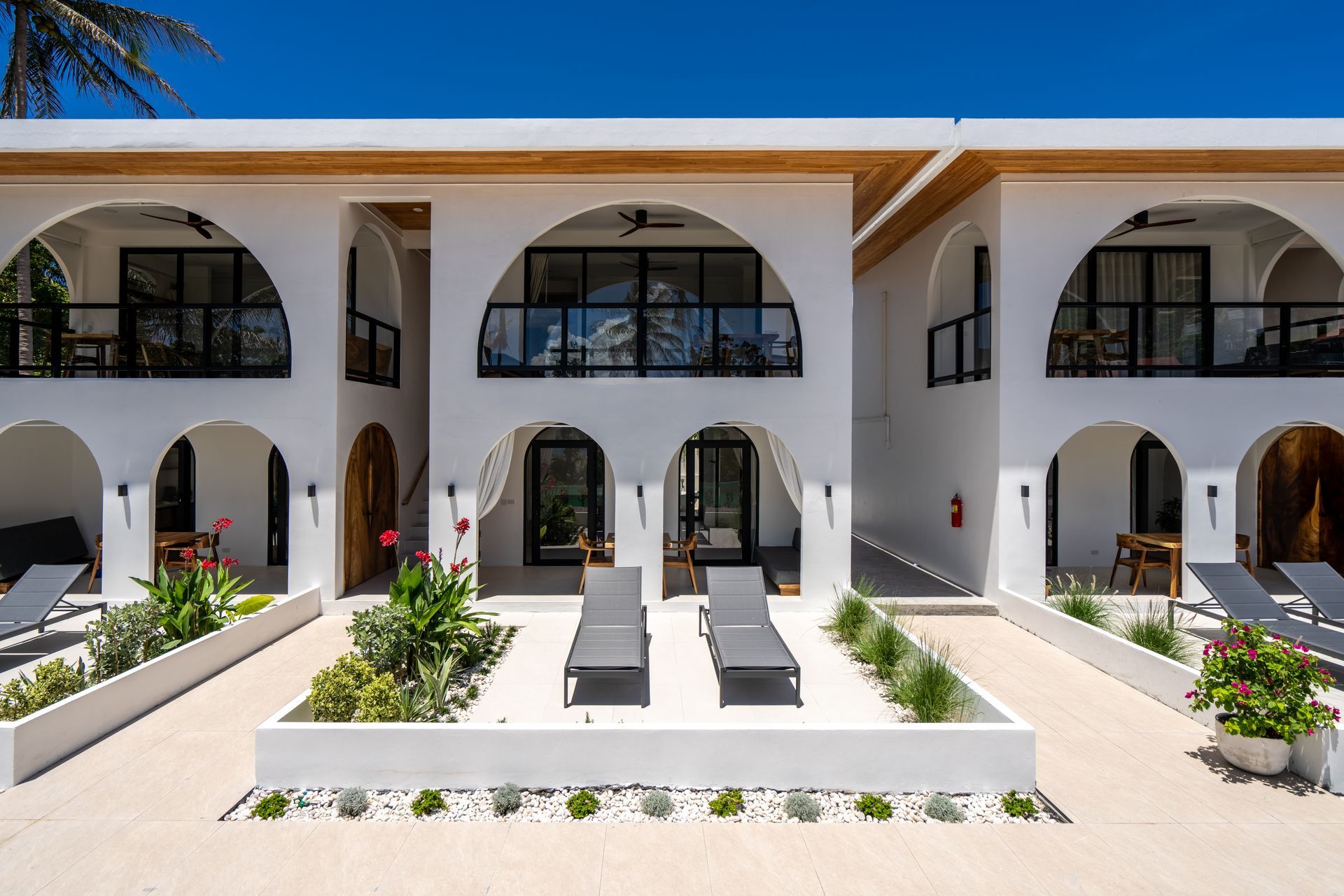 White Mediterranean-style courtyard with arches, lounge chairs, and potted plants under bright sun