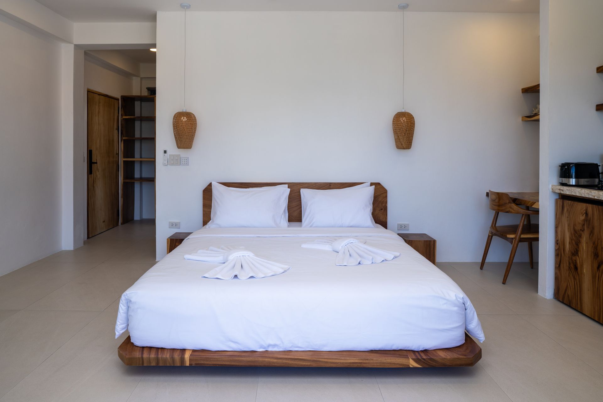 Minimalist bedroom with a low wooden bed, white linens, and wicker wall decor