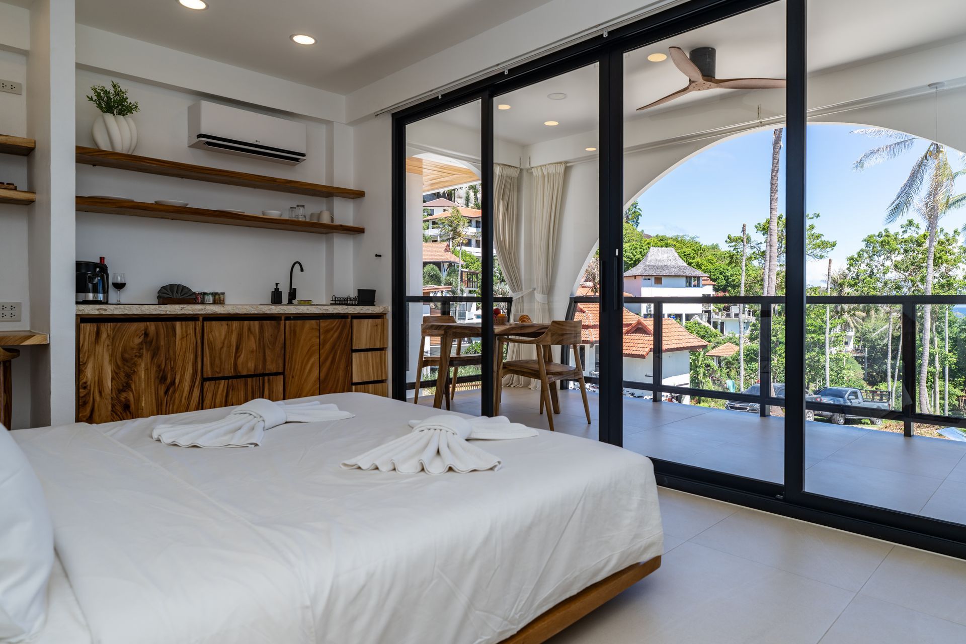 Bright bedroom with king bed and open sliding doors to a balcony and tropical pool view