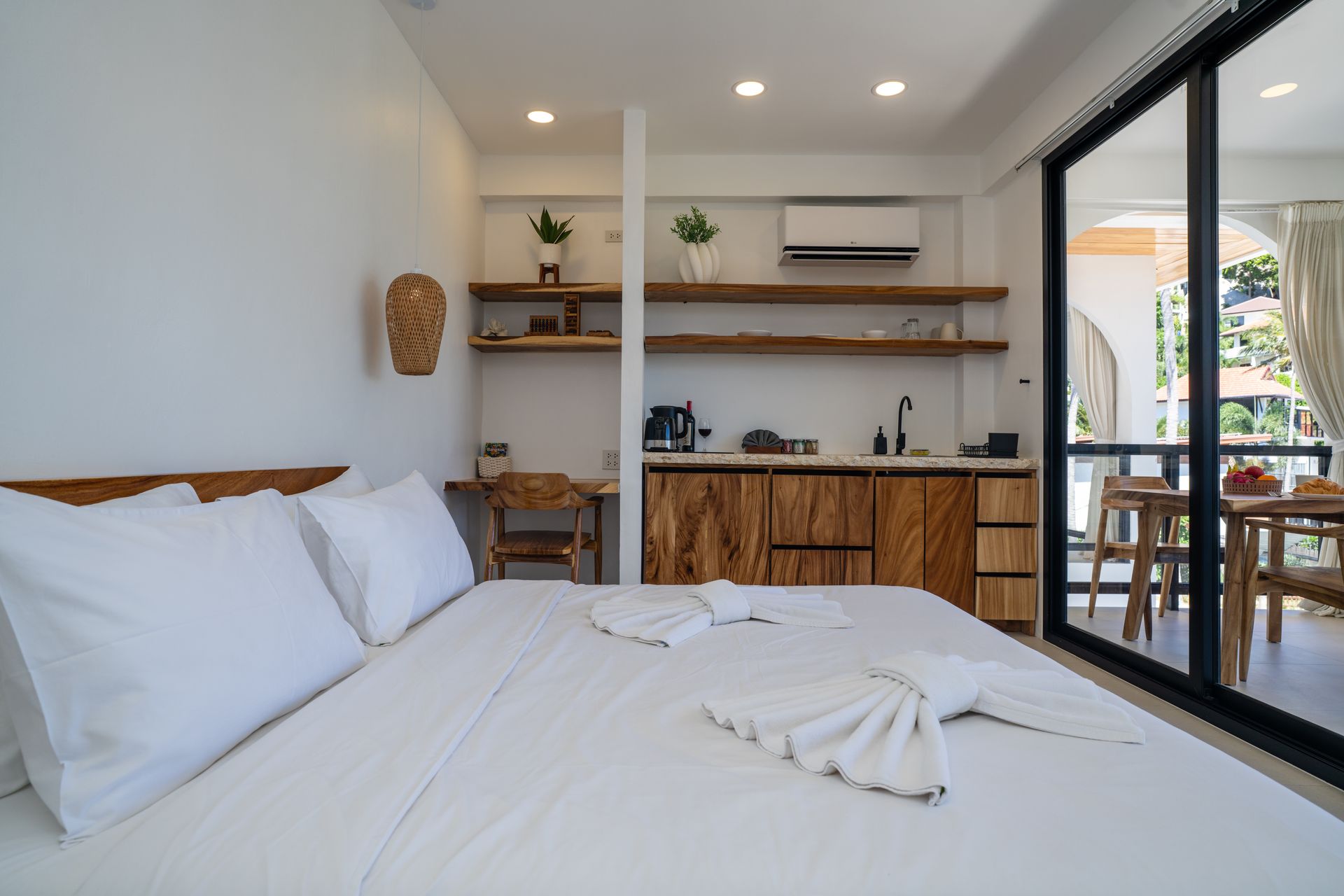 Minimal white bedroom with a bed, kitchenette, and sliding glass door to a patio