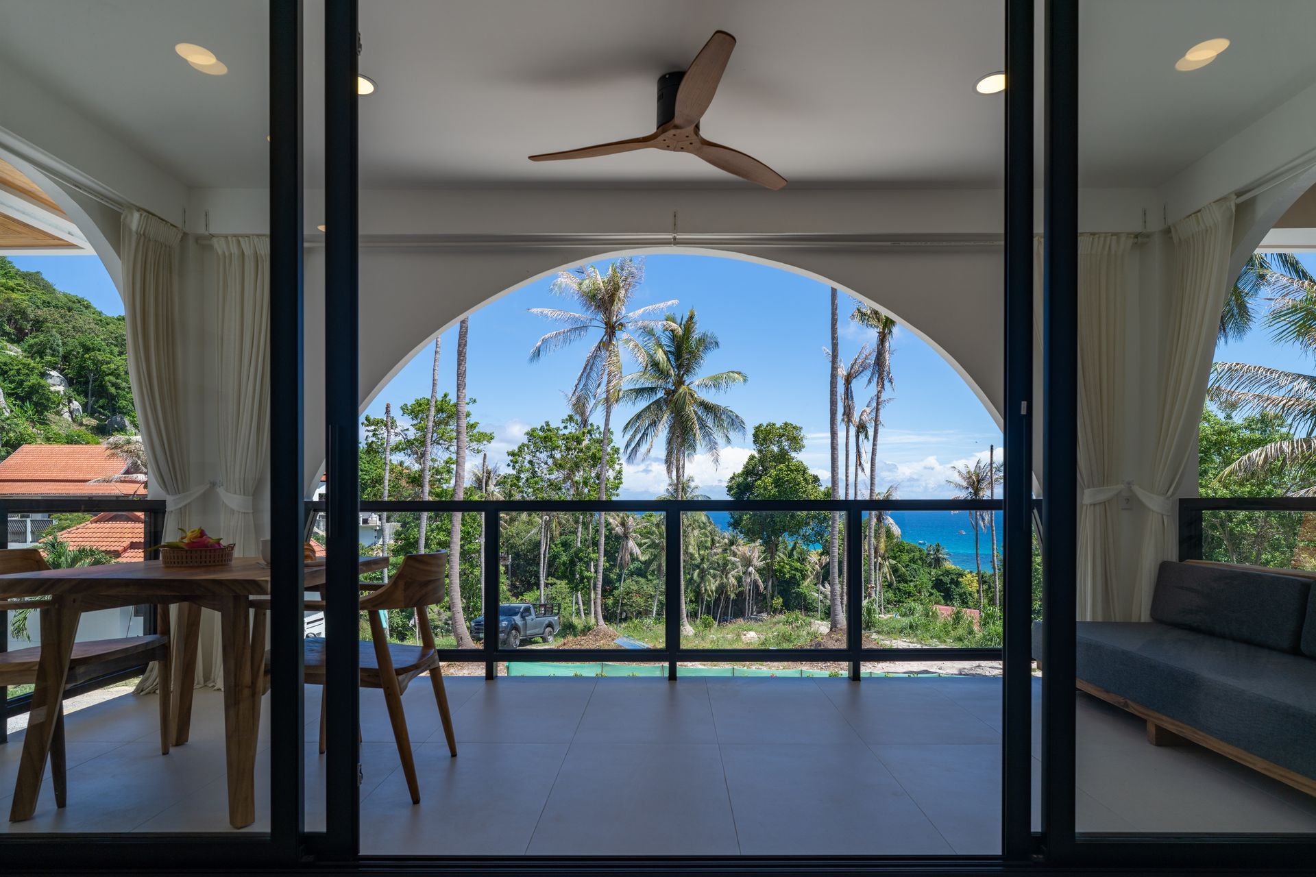 Modern patio with glass doors, ceiling fan, and ocean-view balcony framed by palm trees.