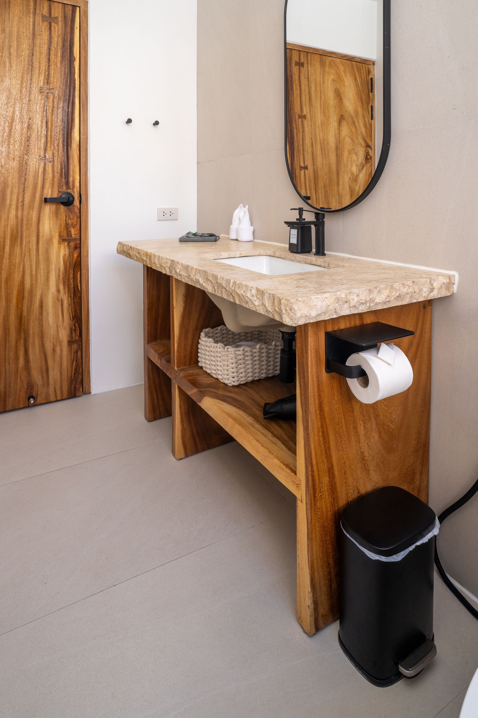 Rustic wood bathroom vanity with stone sink, mirror, towel shelf, and black trash bin