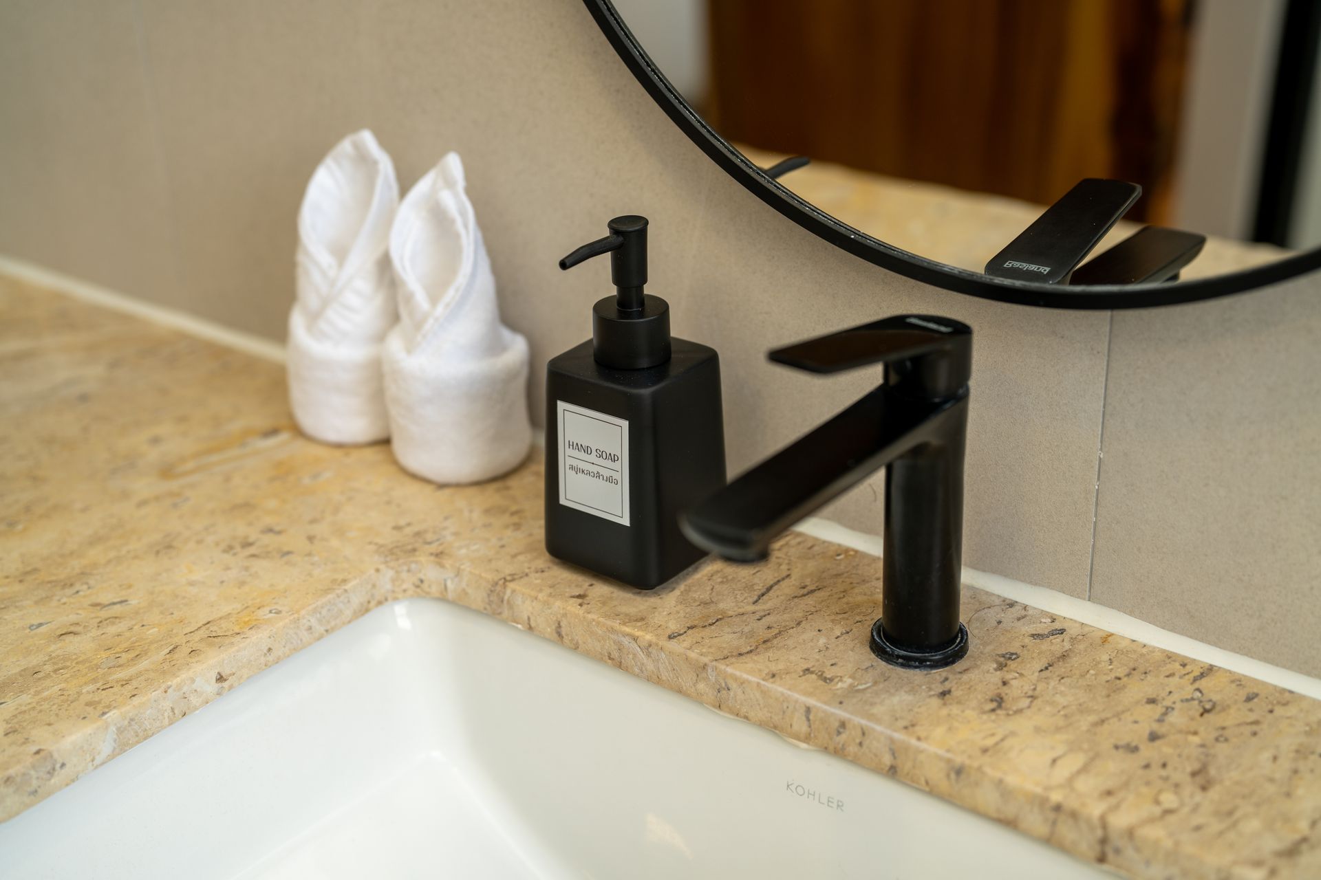 Bathroom sink with black faucet and soap dispenser on a beige countertop, with folded white towels nearby