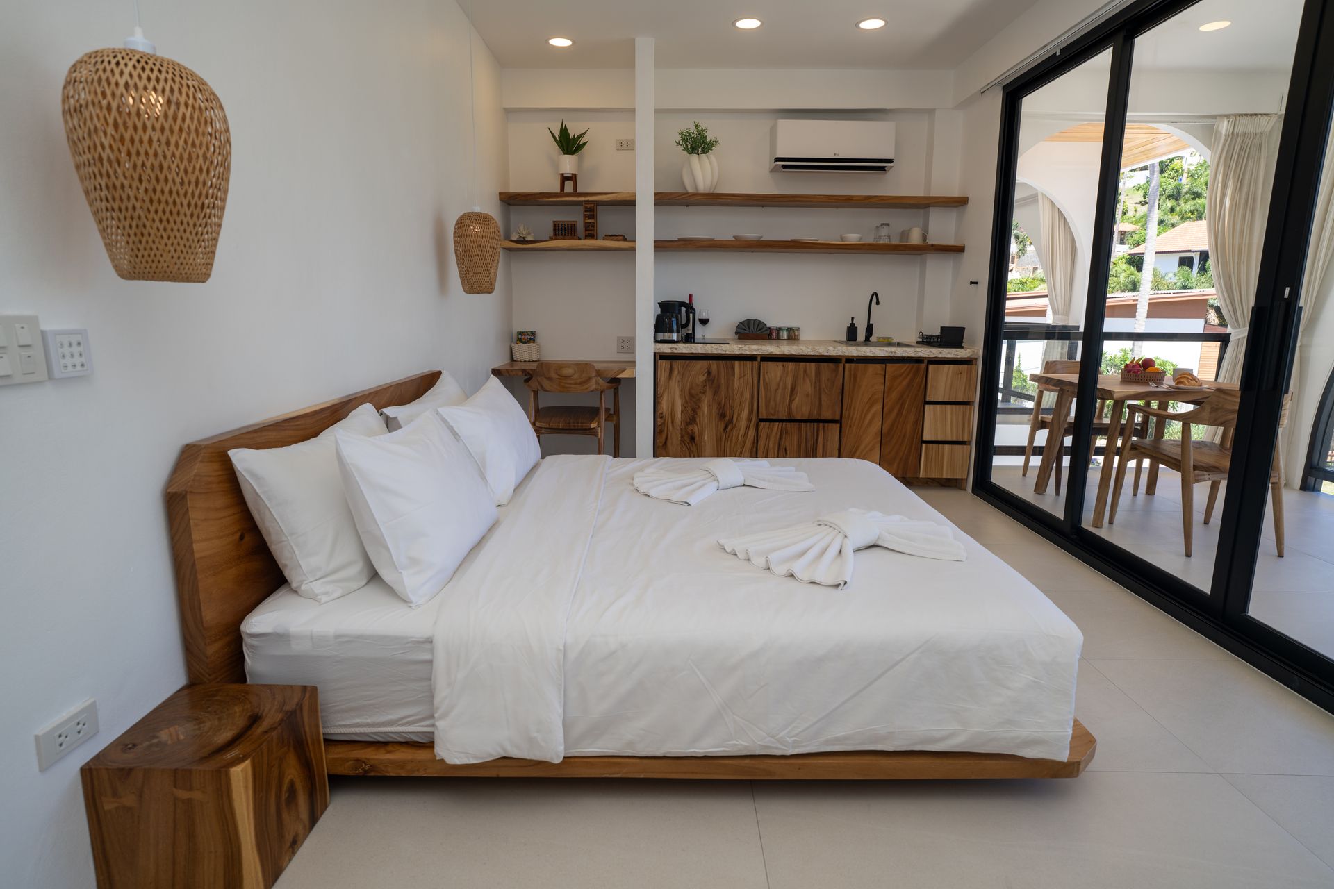 Bright modern bedroom with a white bed, wooden accents, open shelves, and sliding glass doors to a balcony