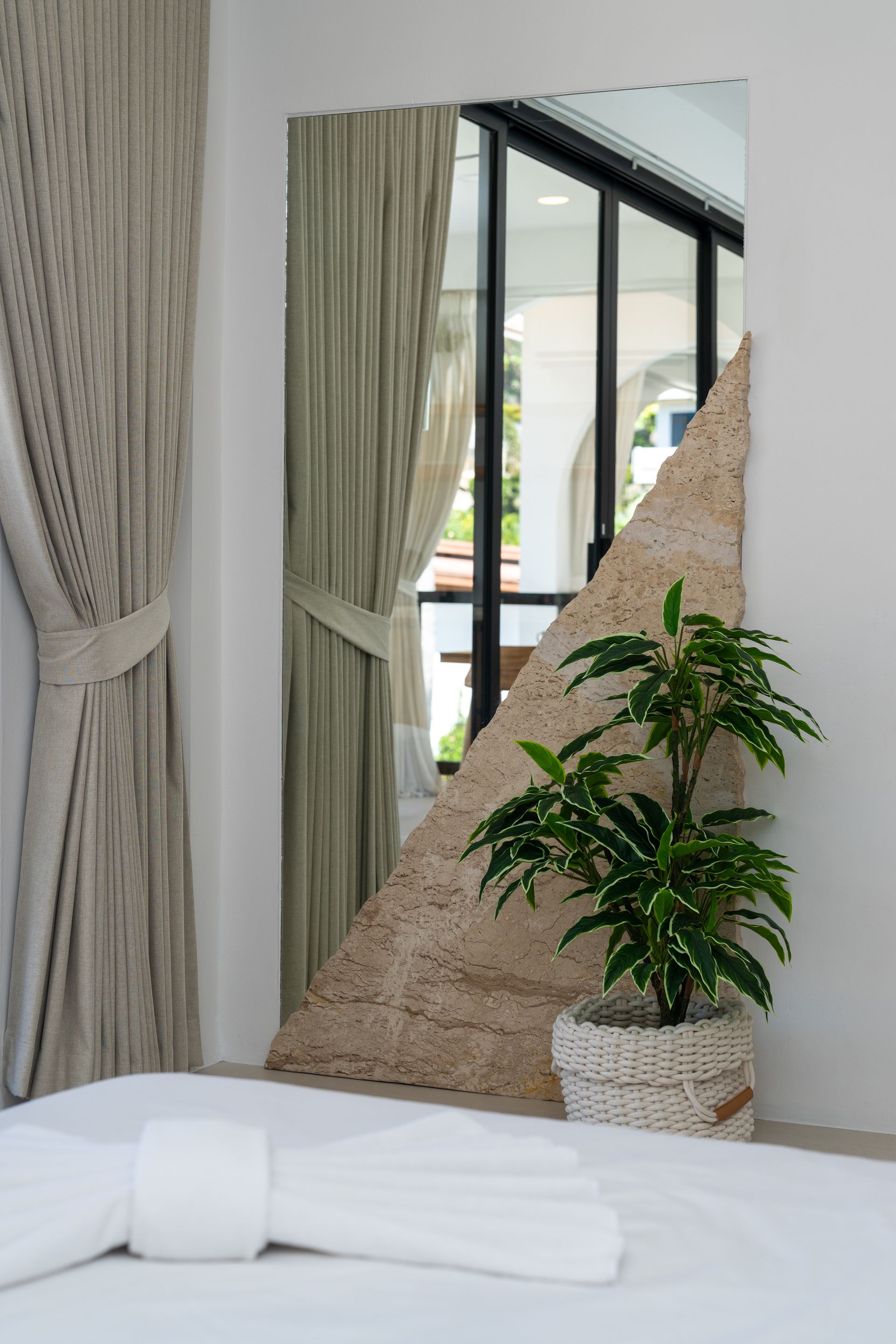 White bed with folded towels, potted plant, and tall mirror in a bright modern bedroom
