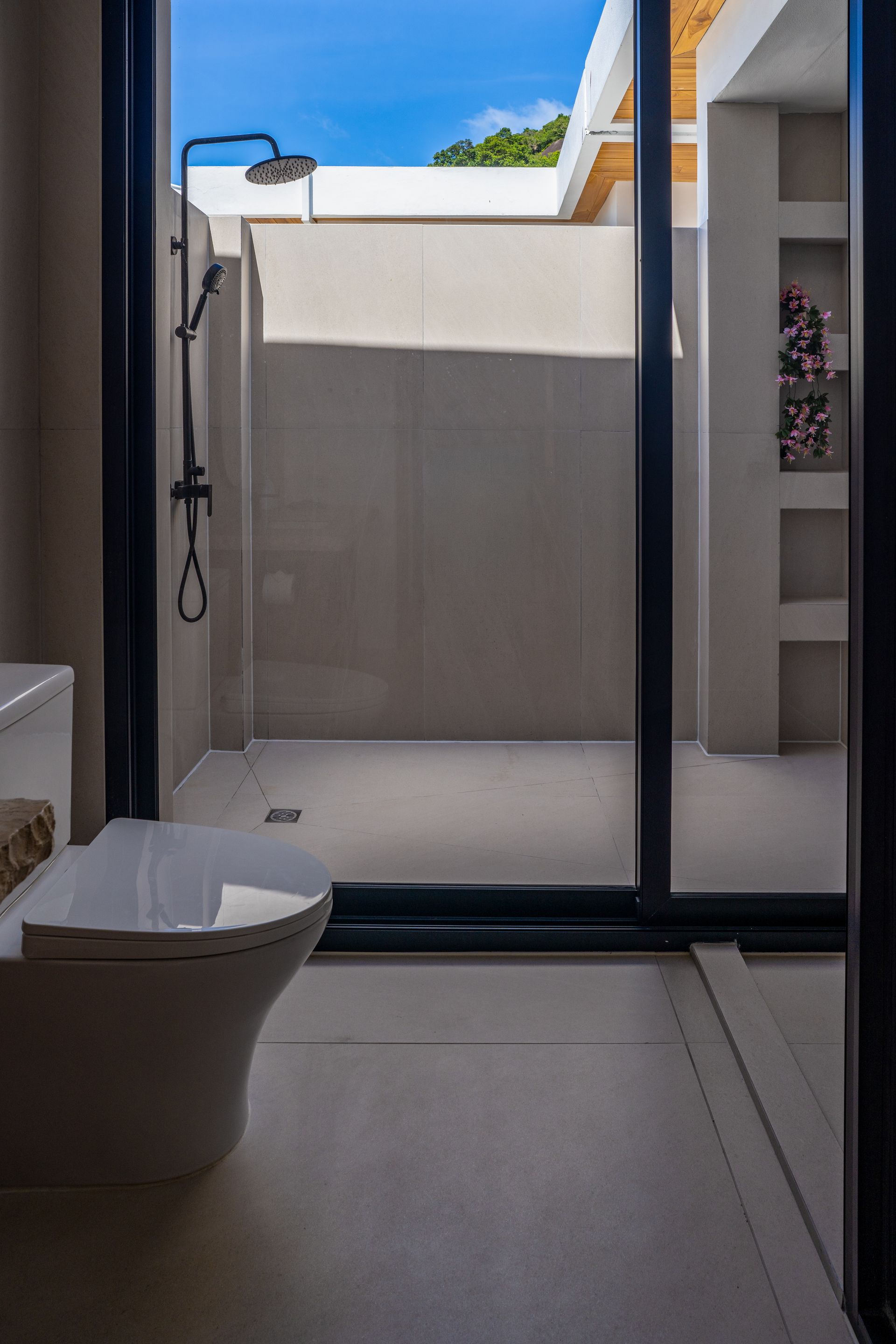 Modern bathroom with walk-in shower, glass door, and white sink beside a sunlit patio view