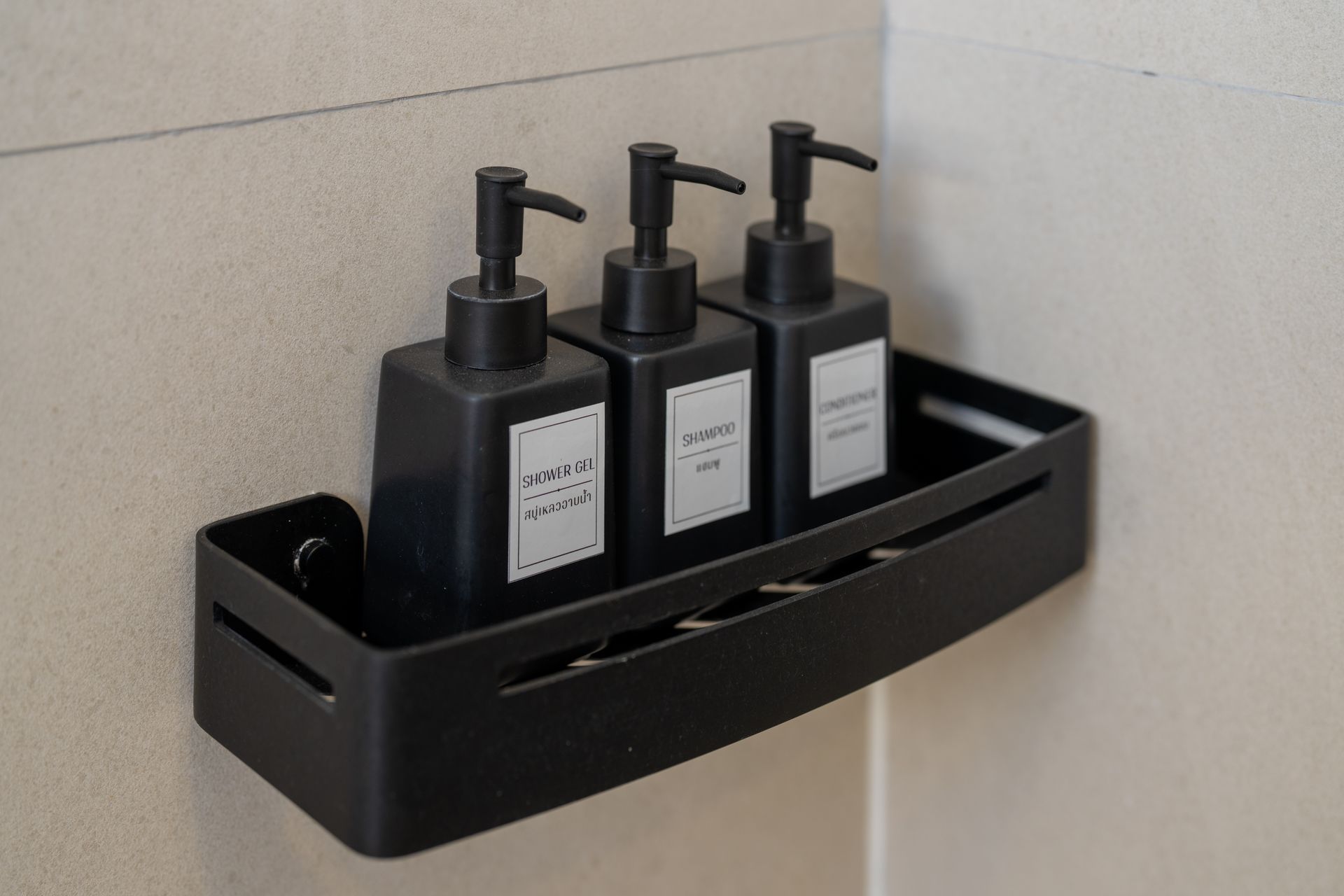 Black wall-mounted shower caddy holding three black pump bottles against beige tile