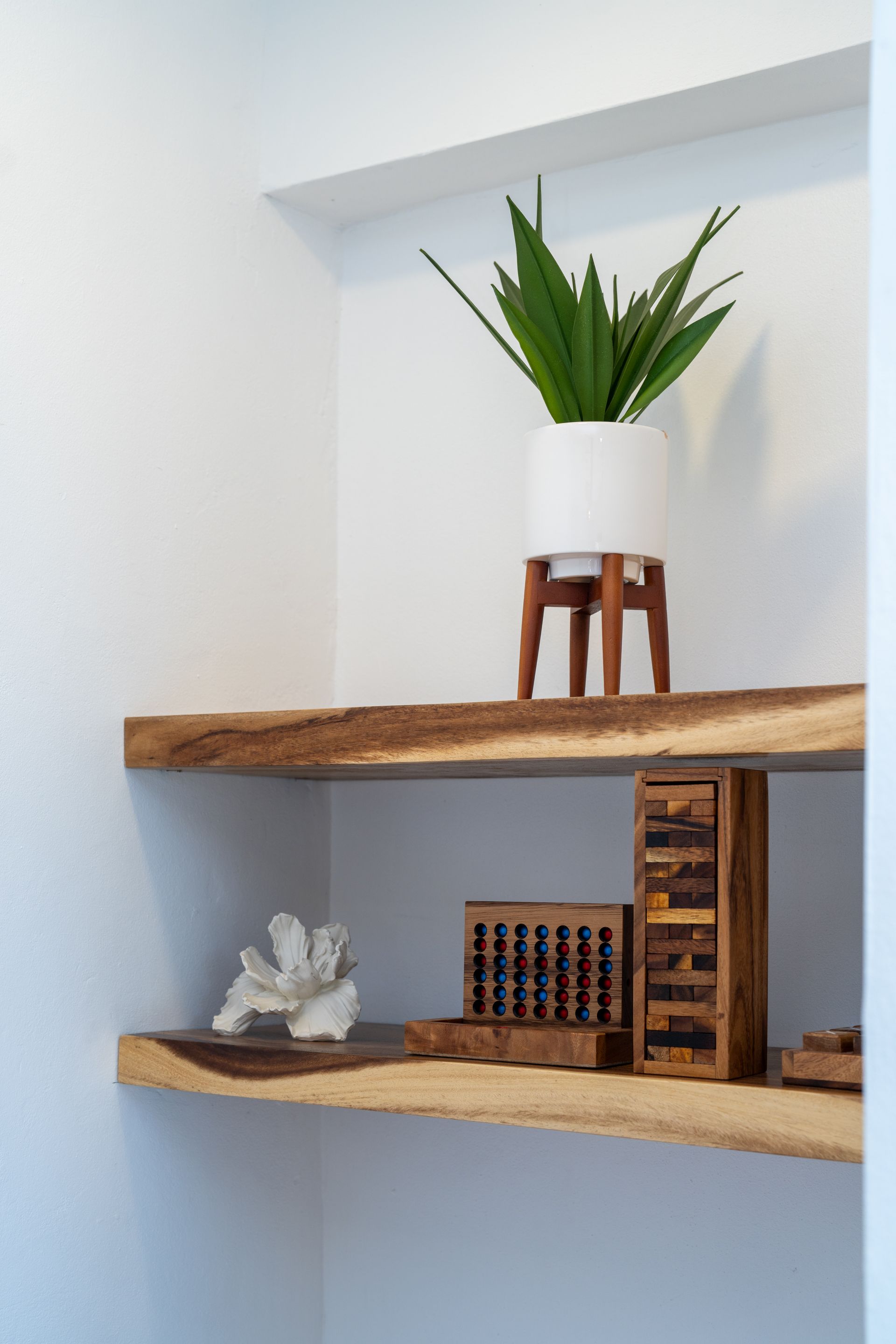 Wooden wall shelves with a white planter, small decor pieces, and a potted plant on the top shelf