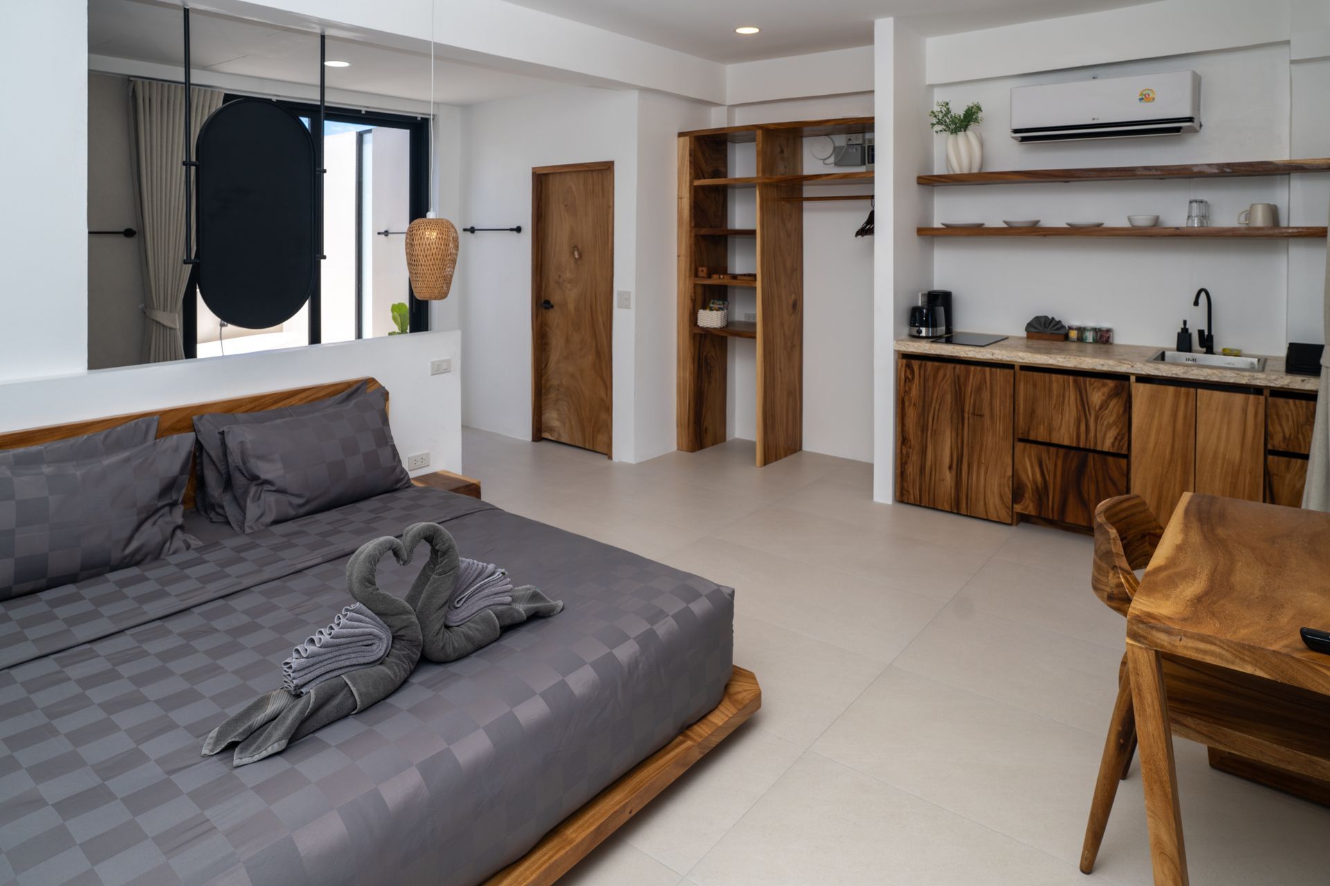 Modern studio bedroom with gray bed, wooden furniture, desk, and kitchenette nook