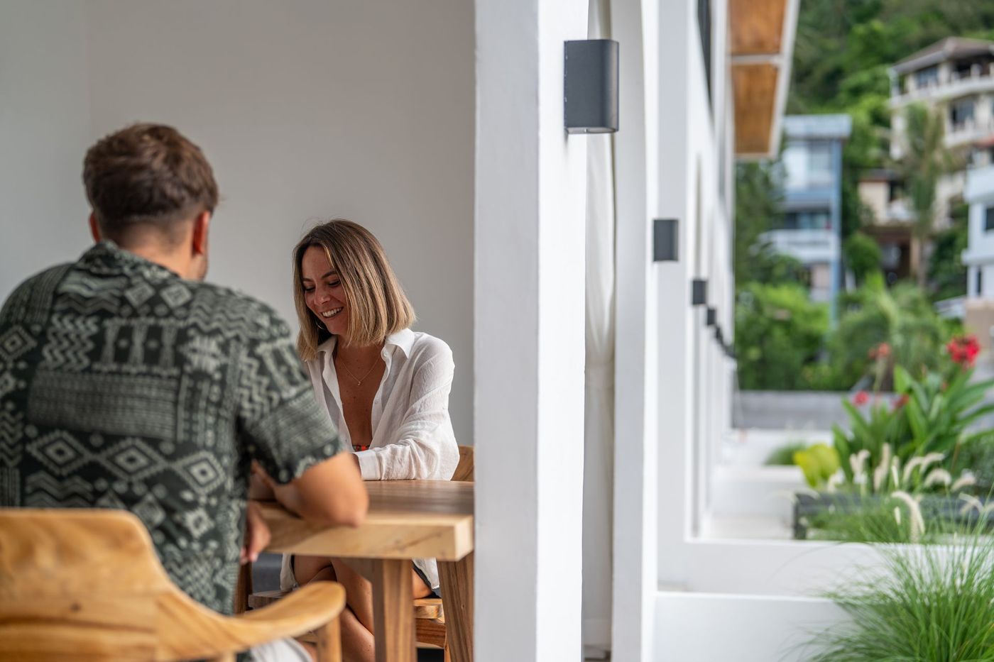 Two people talking at a wooden table in a bright café by a window overlooking greenery.