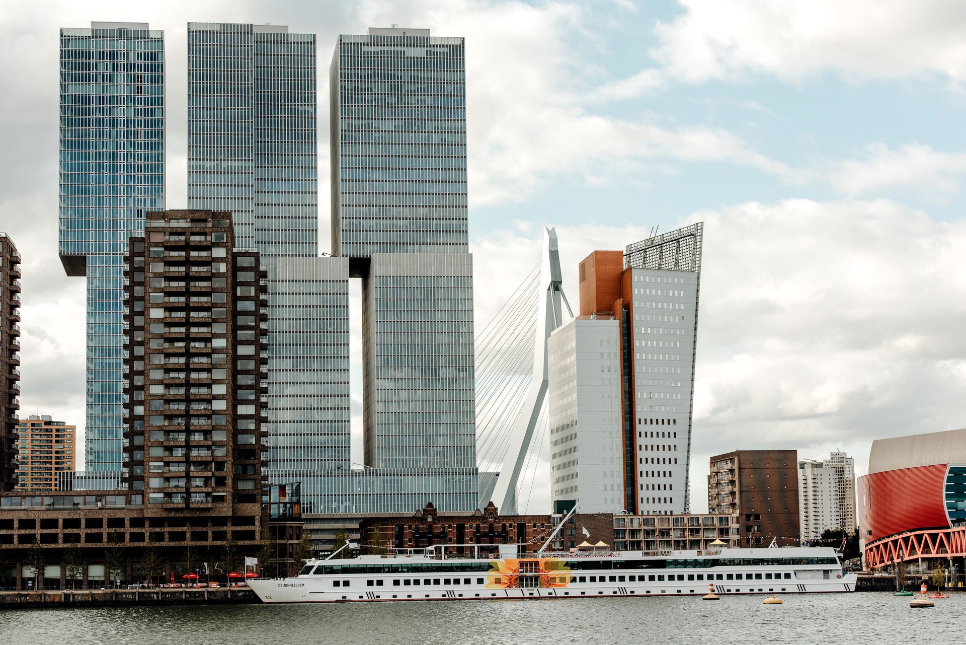 Skyline van Rotterdam met moderne, gedraaide wolkenkrabbers, een cruiseschip en een bewolkte lucht.