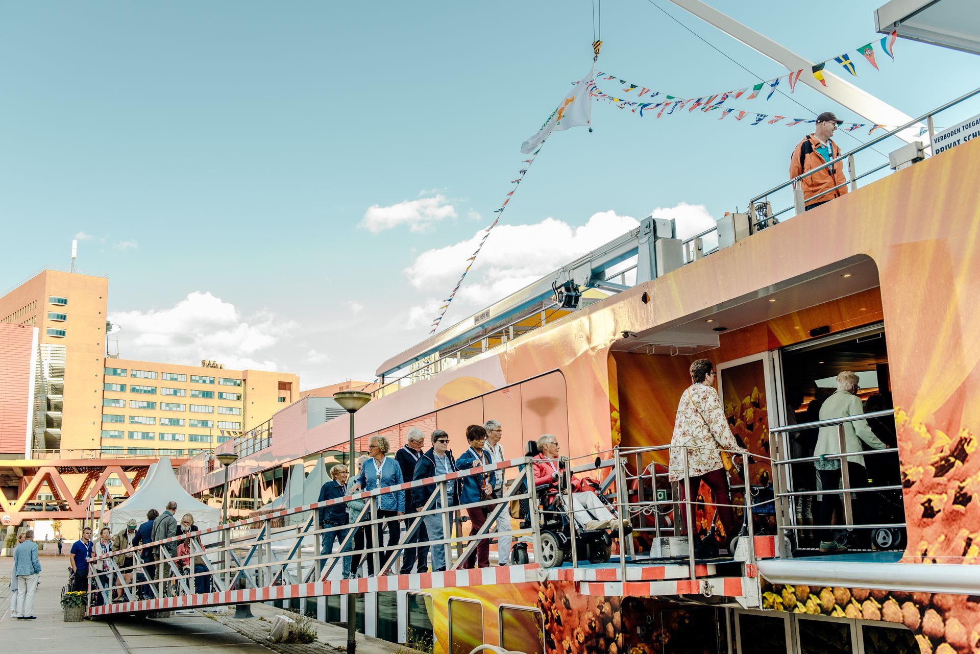 Mensen op een kleurrijke boot met een helling. Gebouwen en de lucht op de achtergrond.