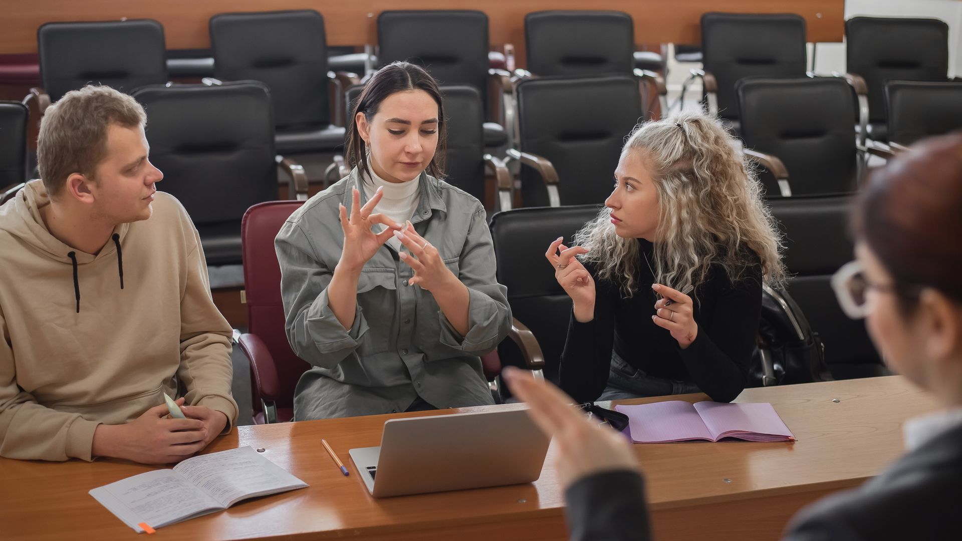 People in a courtroom use sign language. They sit at a table with a laptop, notebooks, and a woman in the foreground.