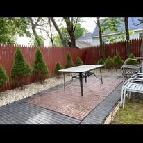 Backyard patio with a table, chairs, red fence, and landscaped border under trees