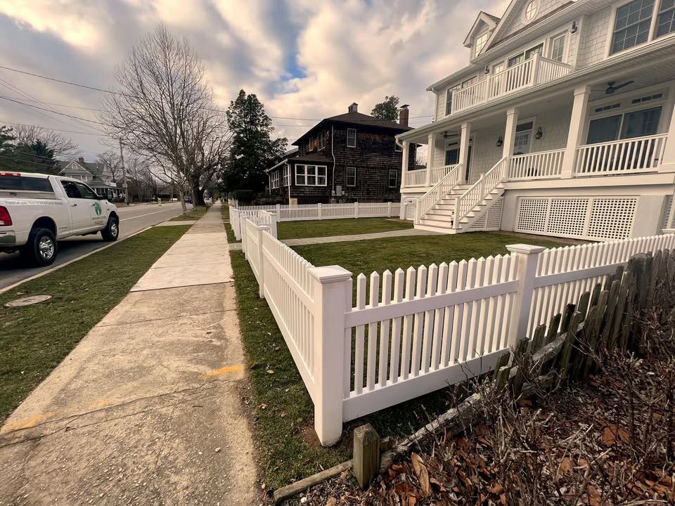 Suburban sidewalk beside white picket fence and white house under a cloudy sky