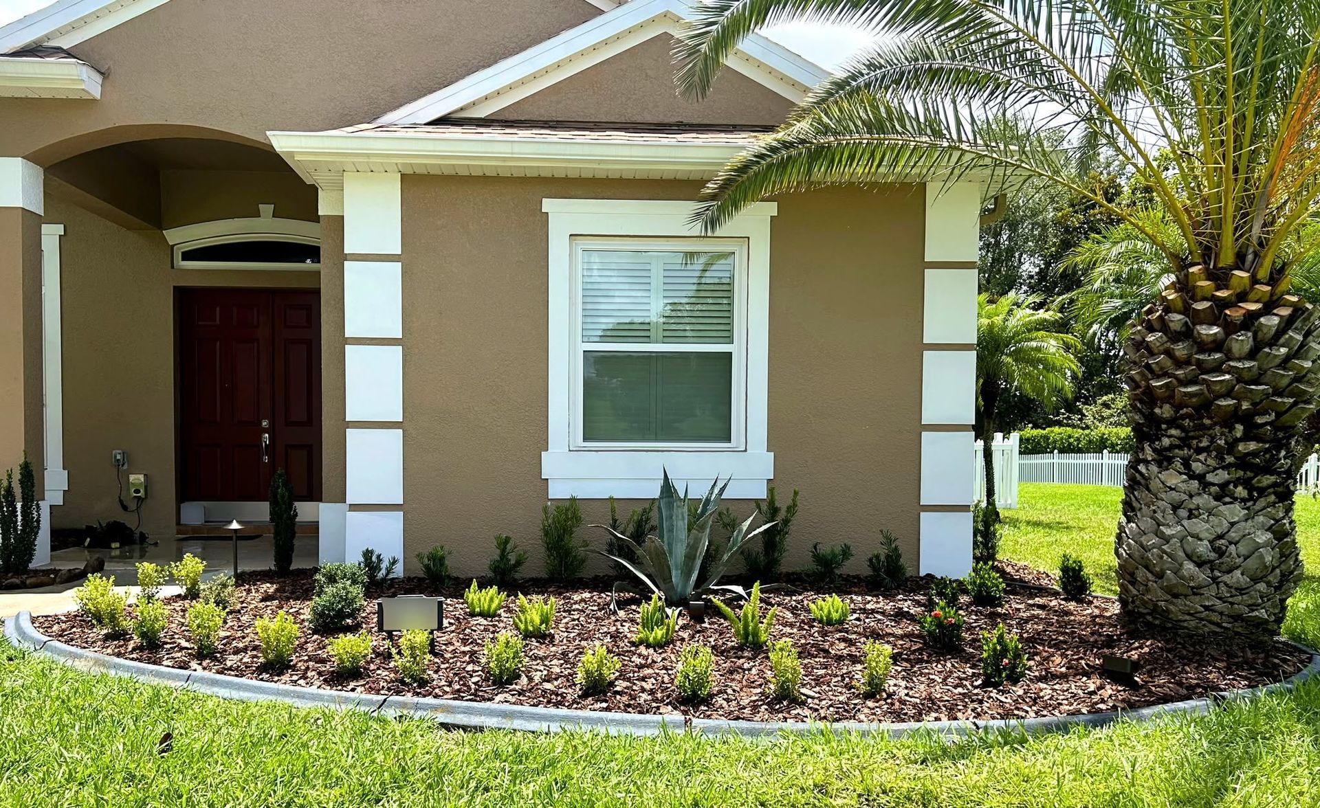 Single-story beige house with white trim, front porch, landscaped garden, and a palm tree in the yard