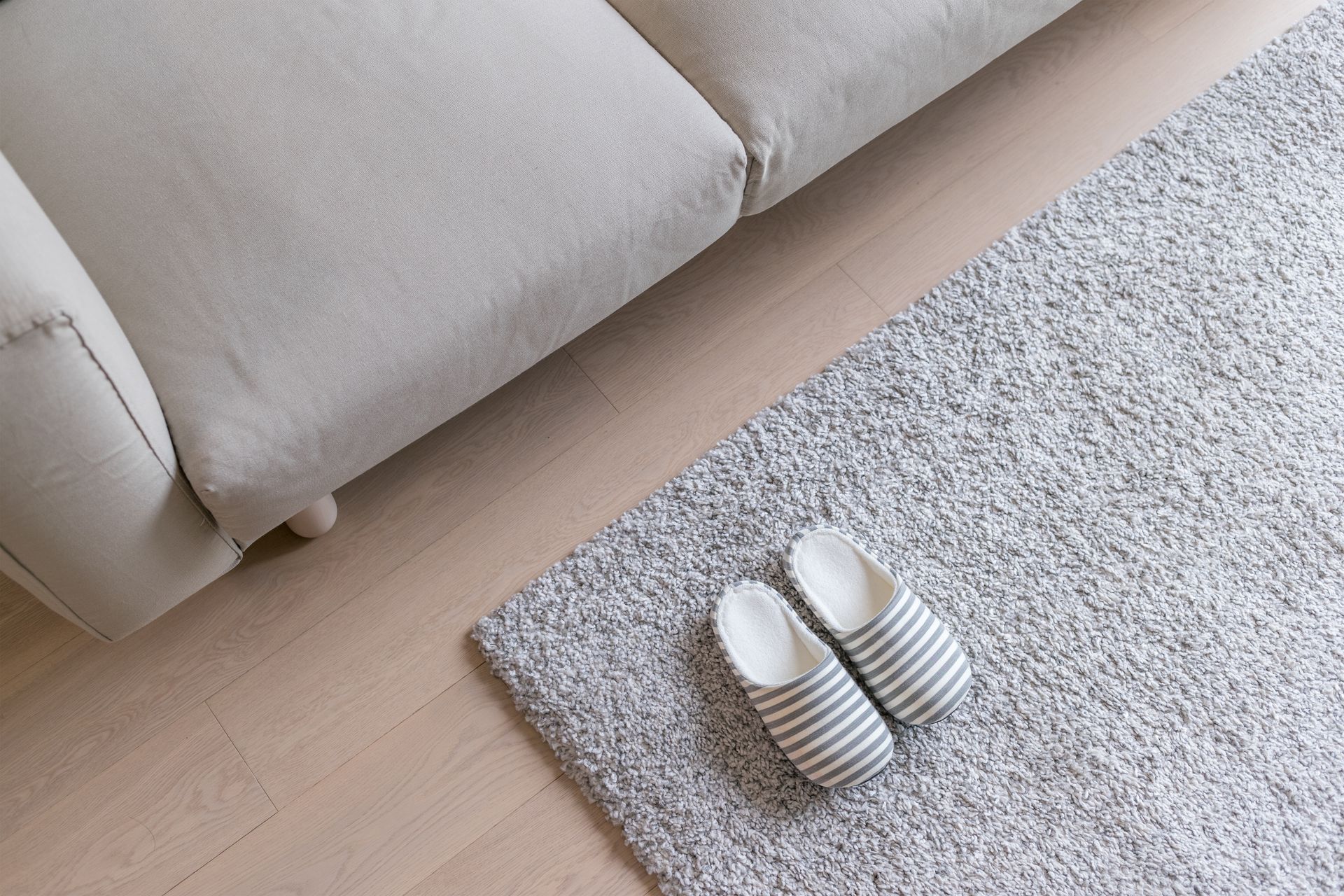 Beige sofa, gray rug with slippers, and light wood flooring.
