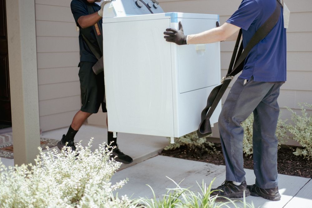 Two Movers Carrying a White Washing Machine out Of a Doorway — Westlake Removals in Morisset, NSW