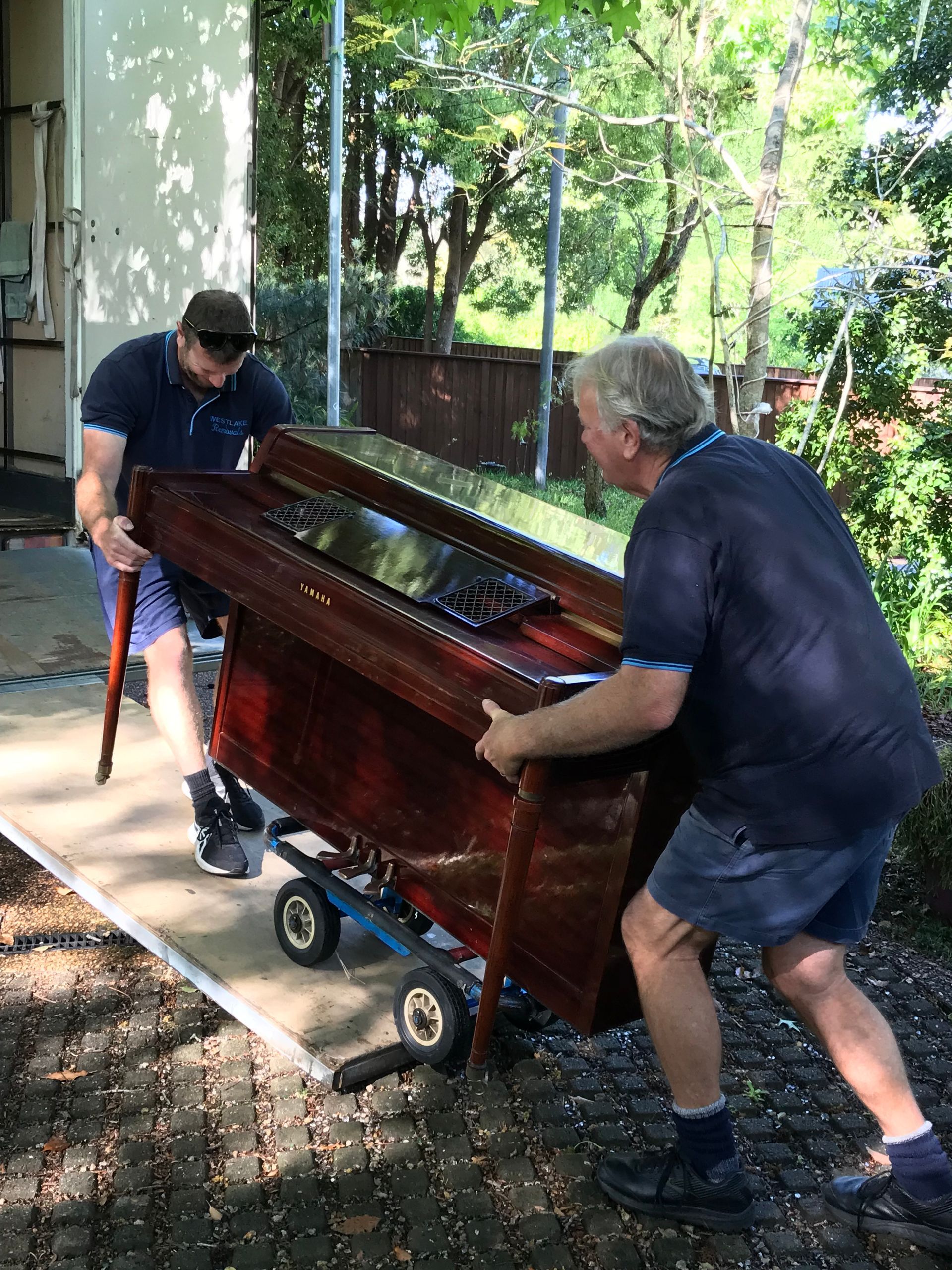 Removalists carefully moving upright piano with trolley during local home move showing safe handling