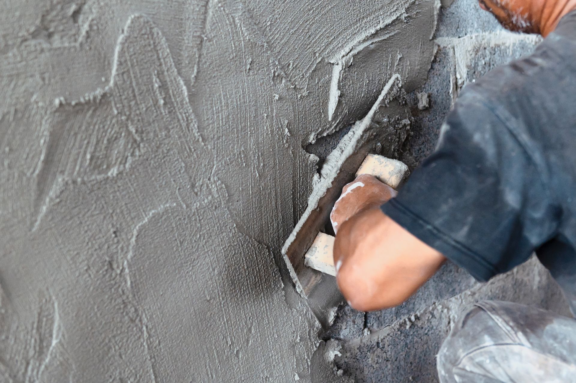 Person glättet grauen Putz an einer Wand mit einer Kelle
