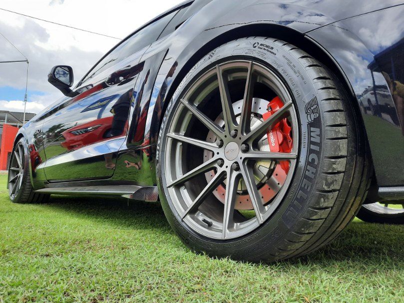 A Black Car With Red Brake Calipers Is Parked On The Grass — Clarence Valley Tyre Centre in South Grafton, NSW