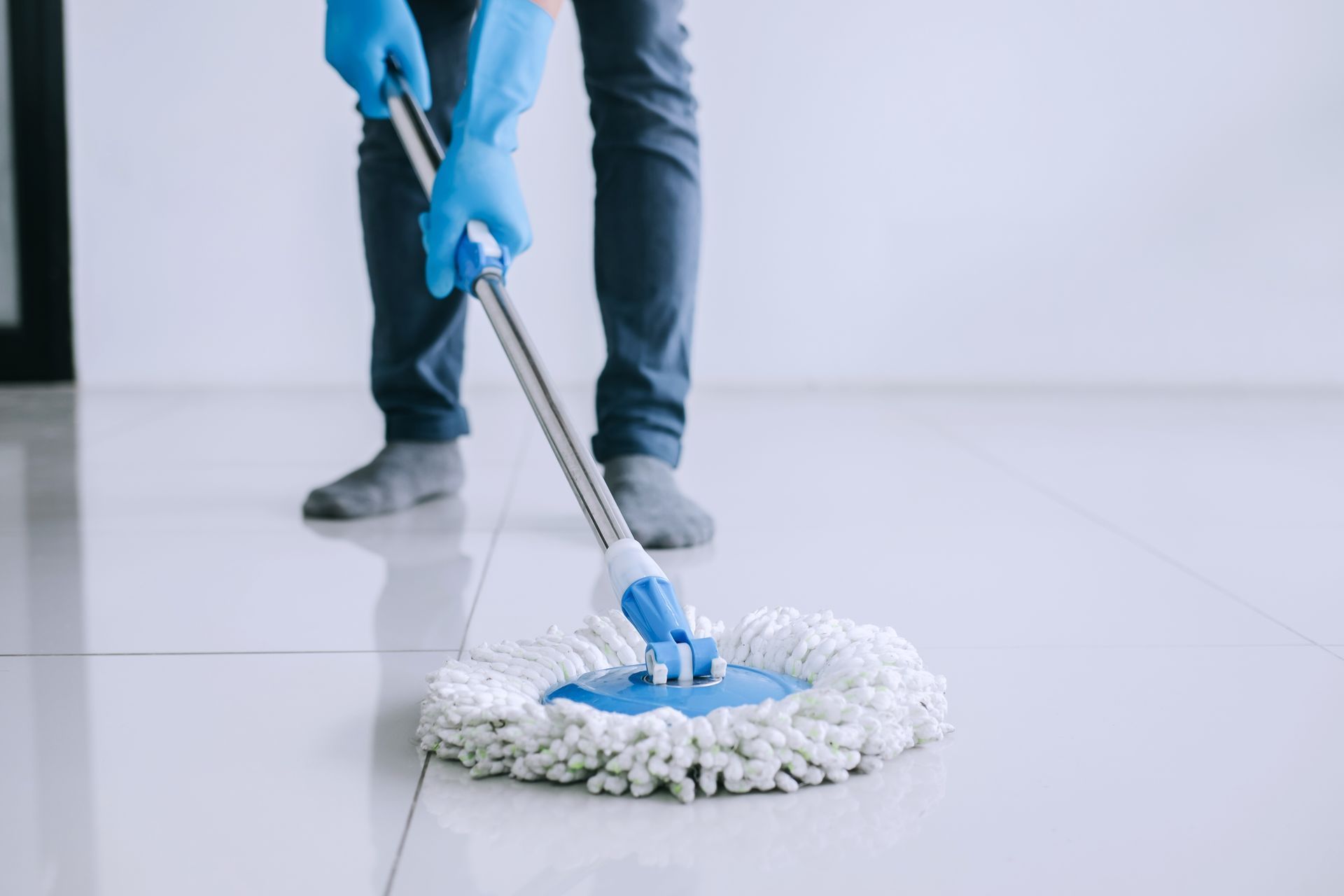Eine Person mit blauen Handschuhen reinigt den Boden mit einem Wischmopp.