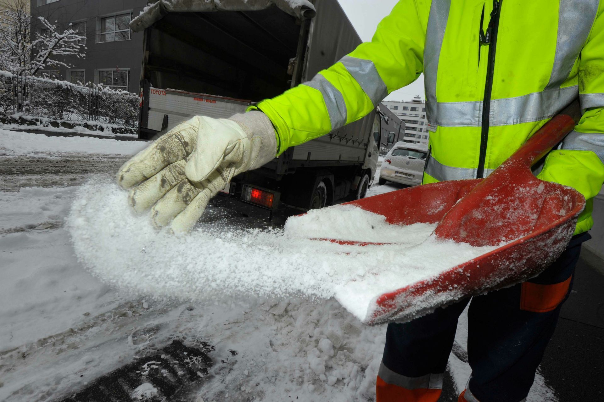 Ein Mann in einer gelben Jacke hält eine rote Schaufel voller Schnee.