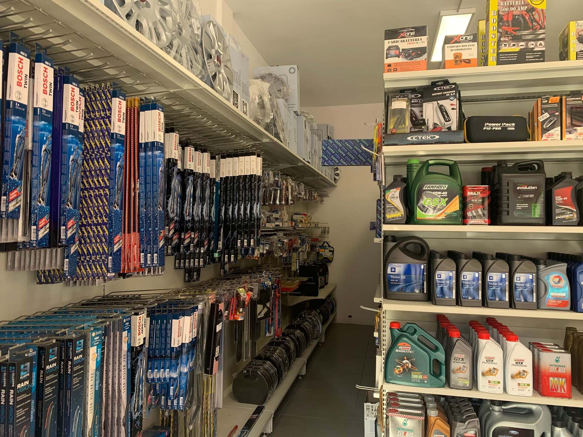 Una corsia di un negozio con scaffali pieni di attrezzi appesi sulla sinistra e fluidi e accessori per auto sulla destra.