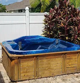 Wooden hot tub with blue cover in a fenced backyard garden
