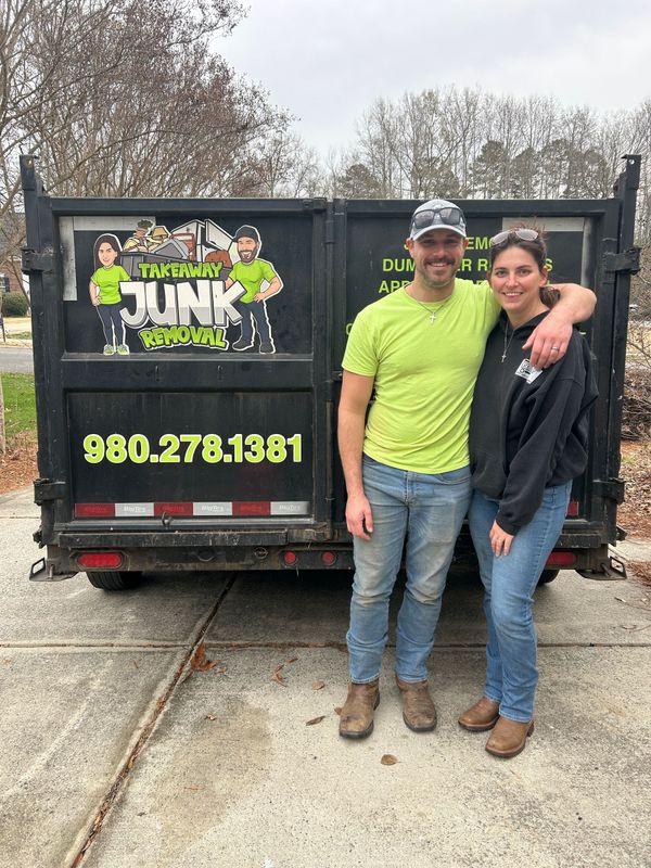 A man and a woman wearing sunglasses are posing for a picture in front of a pile of trash.