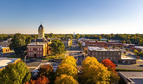 Aerial view of a small downtown with a clock tower, brick buildings, and autumn trees under a clear sky
