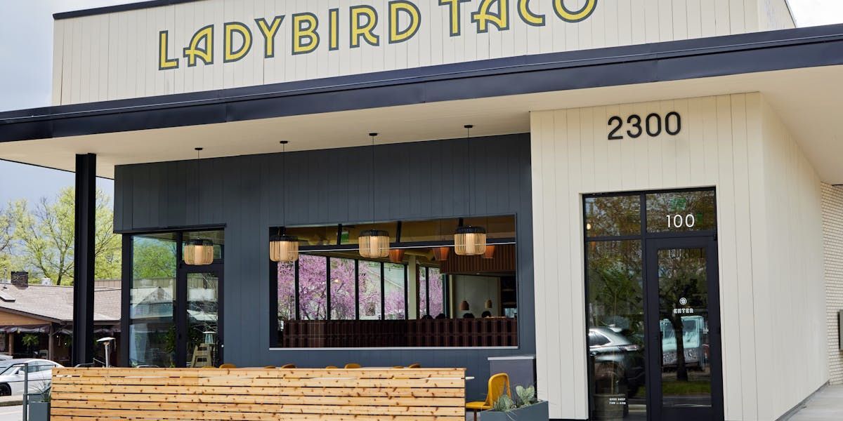 A modern Ladybird Taco restaurant with a white exterior, dark gray accent wall, and a wooden patio barrier at 2300.