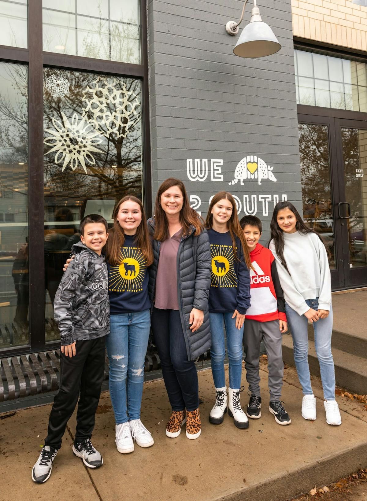 A group of seven people posing together in front of a gray storefront with white text and snowflakes on the window.