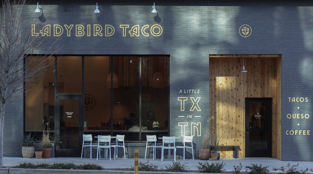 A modern Ladybird Taco restaurant with a white exterior, dark gray accent wall, and a wooden patio barrier at 2300.