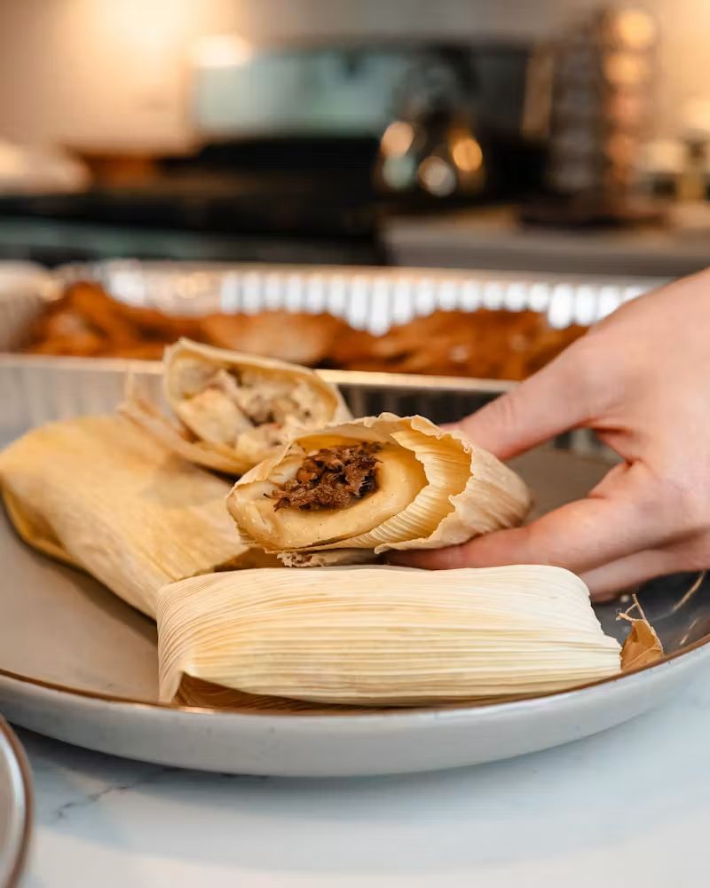Hand placing assorted tamales on a plate at a kitchen counter