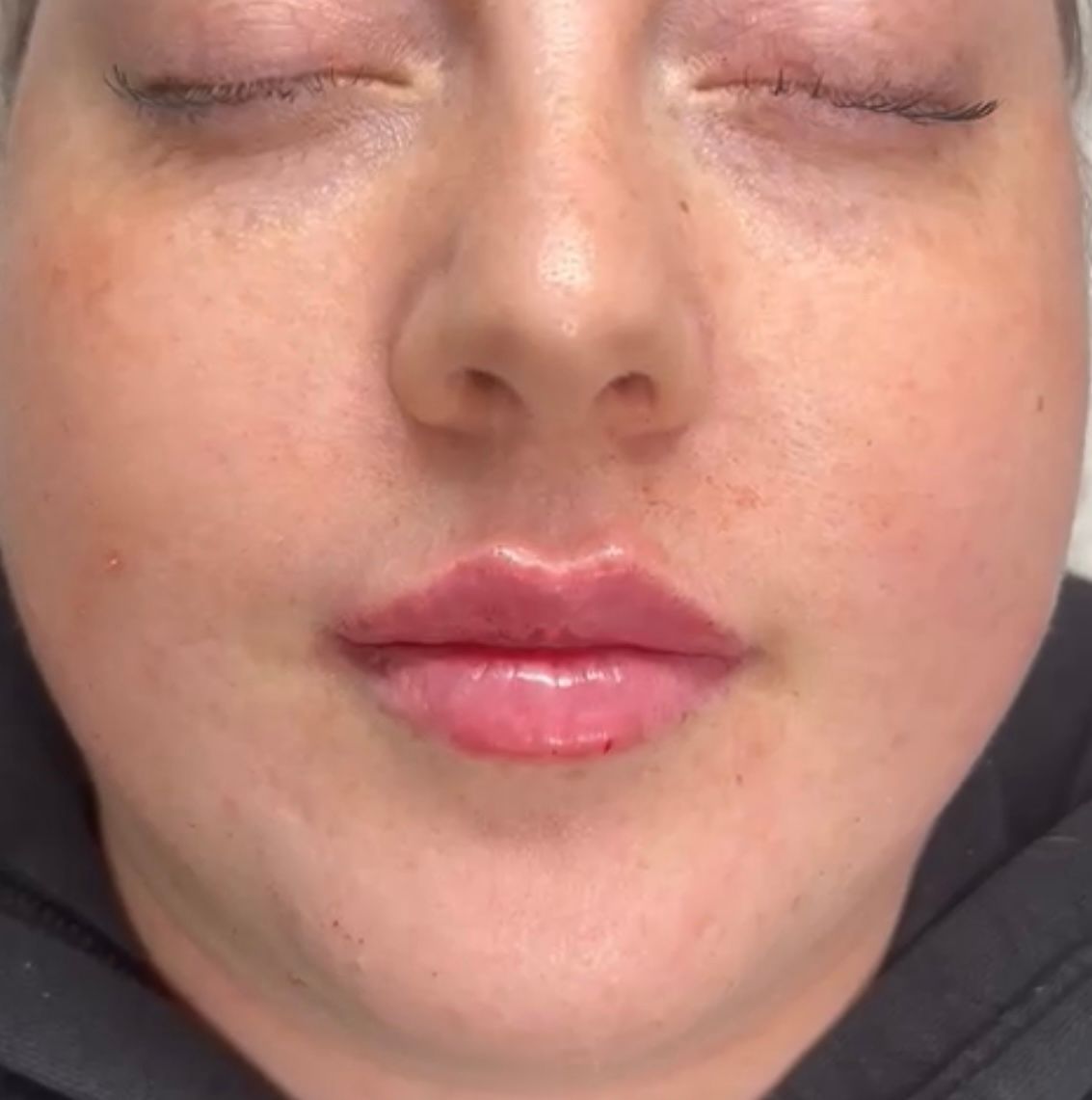 Close-up of a person’s face with closed eyes and glossy pink lips