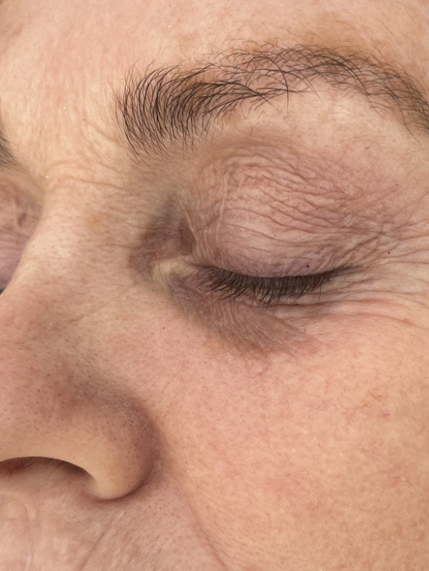 Close-up of a closed eye with a slight wrinkle and natural eyebrow.