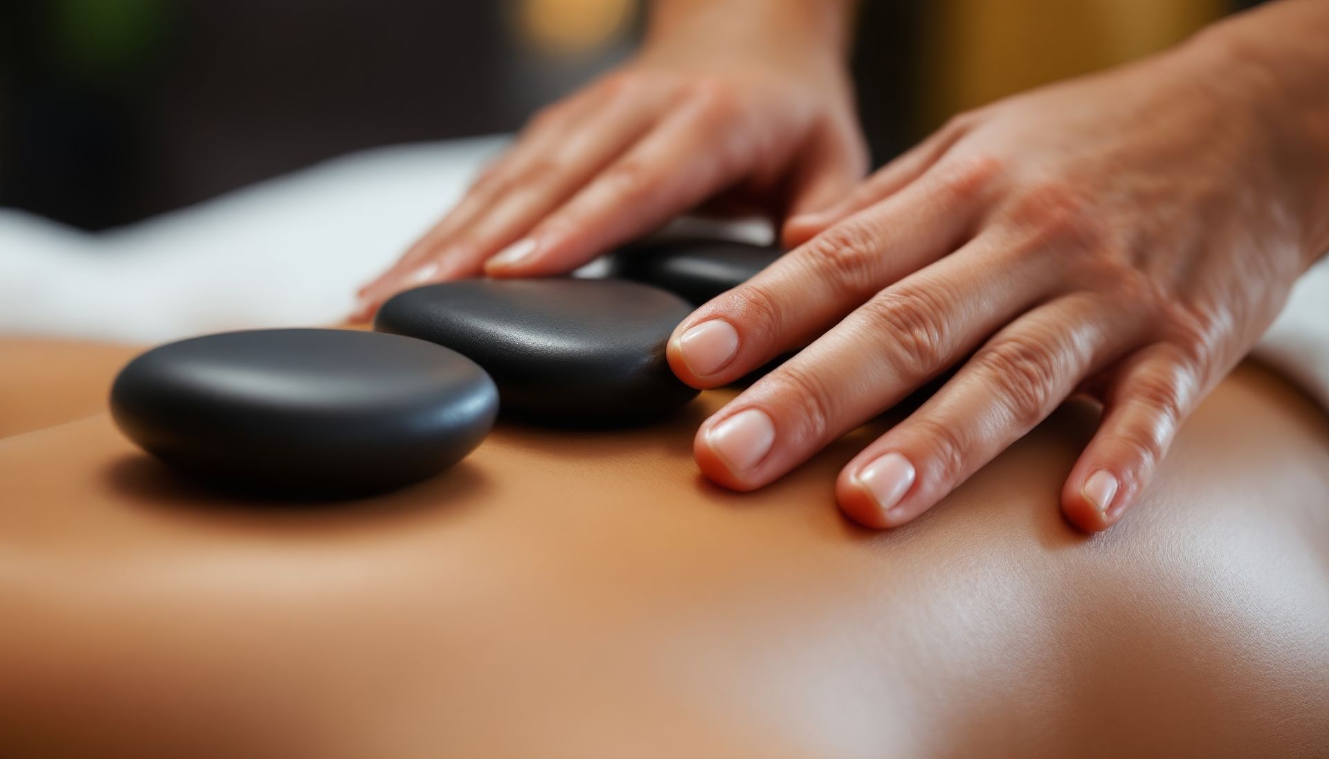 Hands placing hot stones on a person’s bare back during a massage