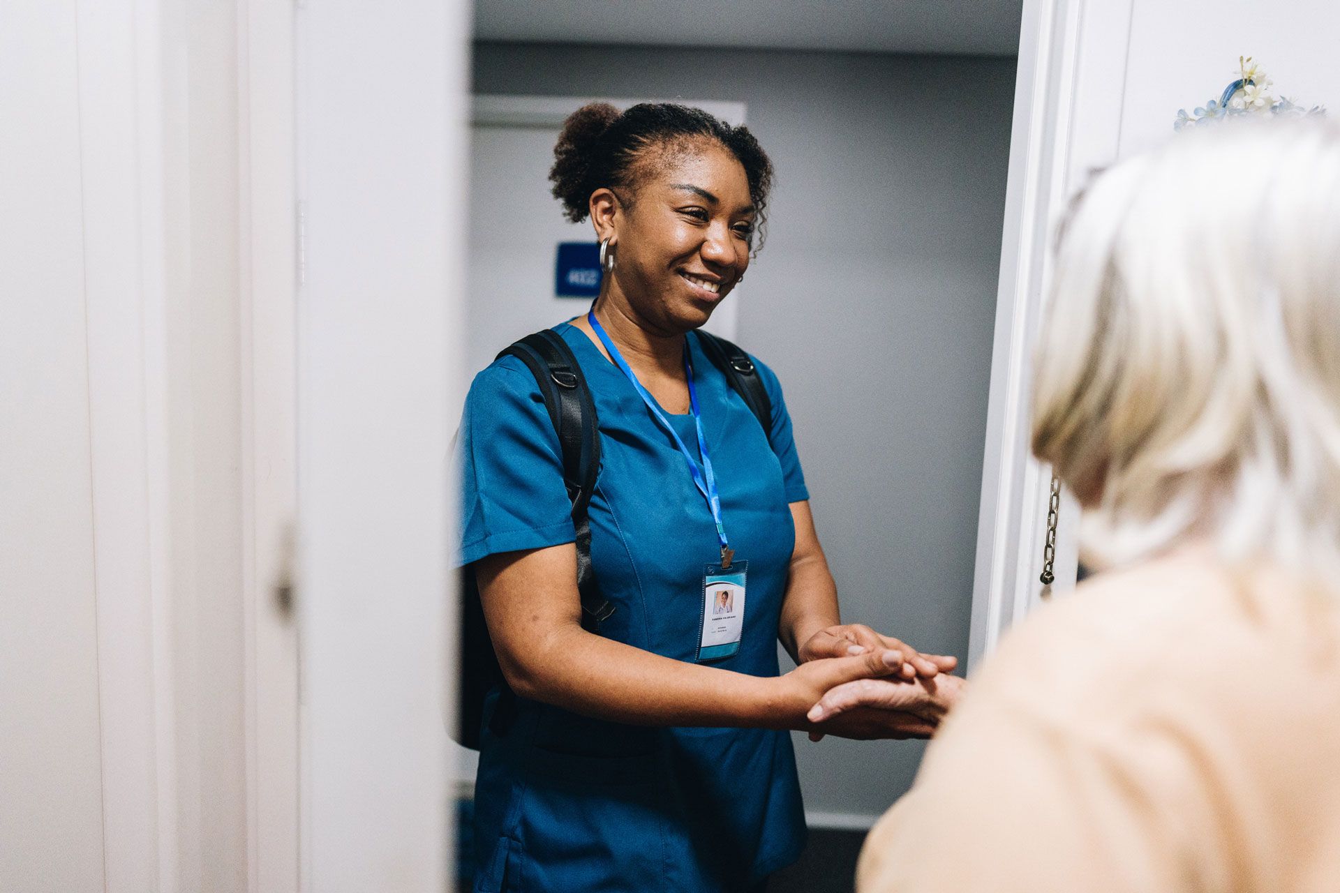 A nurse is shaking hands with an elderly woman in a doorway.