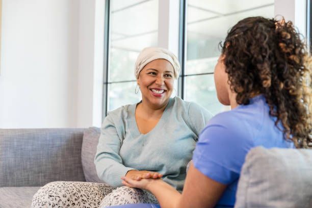 A woman with cancer is sitting on a couch talking to a nurse.