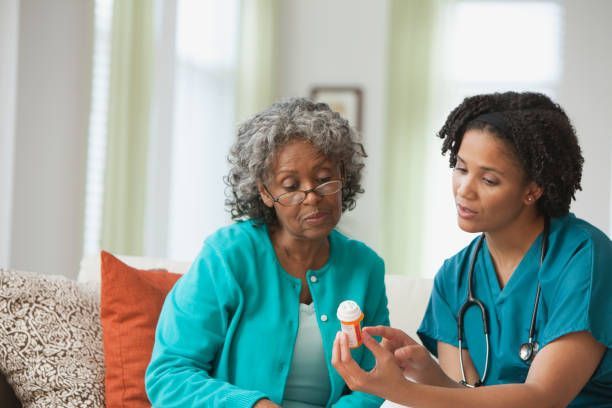 A nurse is showing an elderly woman a bottle of pills.