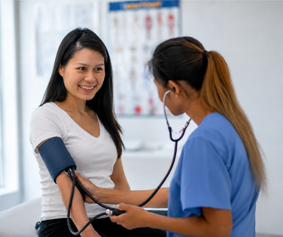 Nurse taking a woman’s blood pressure in a clinic, with the patient smiling