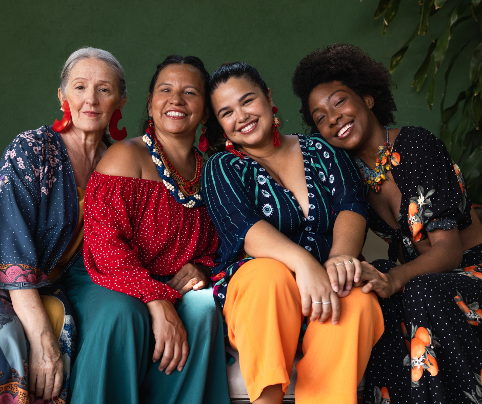Four smiling women seated on a couch, of varying ages and ethnicities.