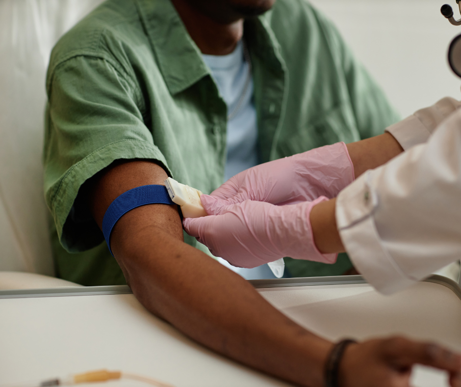 Healthcare worker drawing blood from a seated patient’s arm with a blue tourniquet.