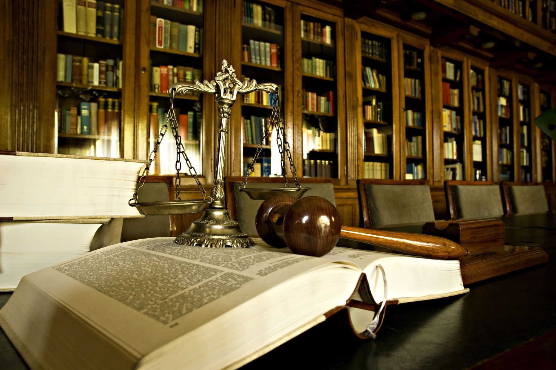 Open law book with scales and gavel on a desk in a warm, book-lined library