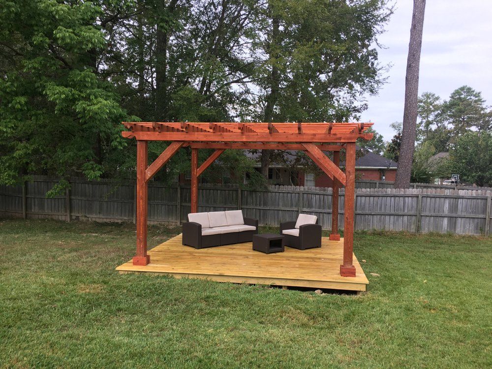 A wooden pergola with a couch and chairs underneath it in a backyard.