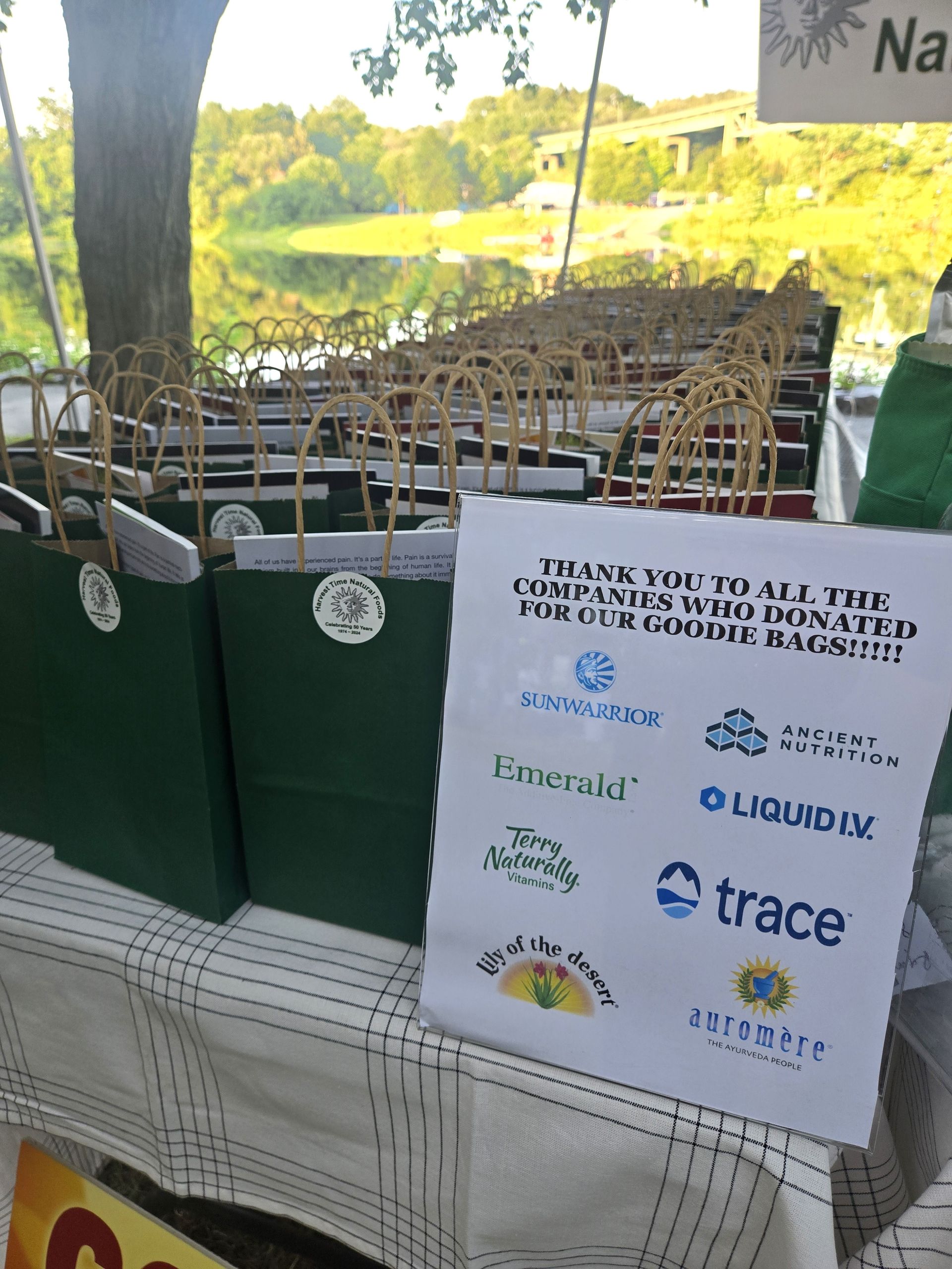 Rows of green gift bags on a table outdoors, with a sign thanking sponsors whose logos are listed below the text.