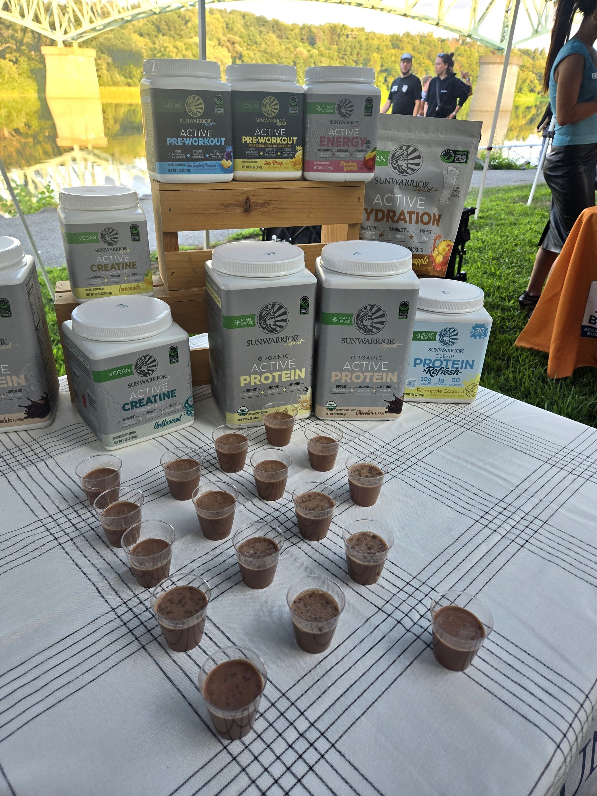 Table display of nutritional supplement canisters with small sample cups arranged in a triangle on a checkered cloth.