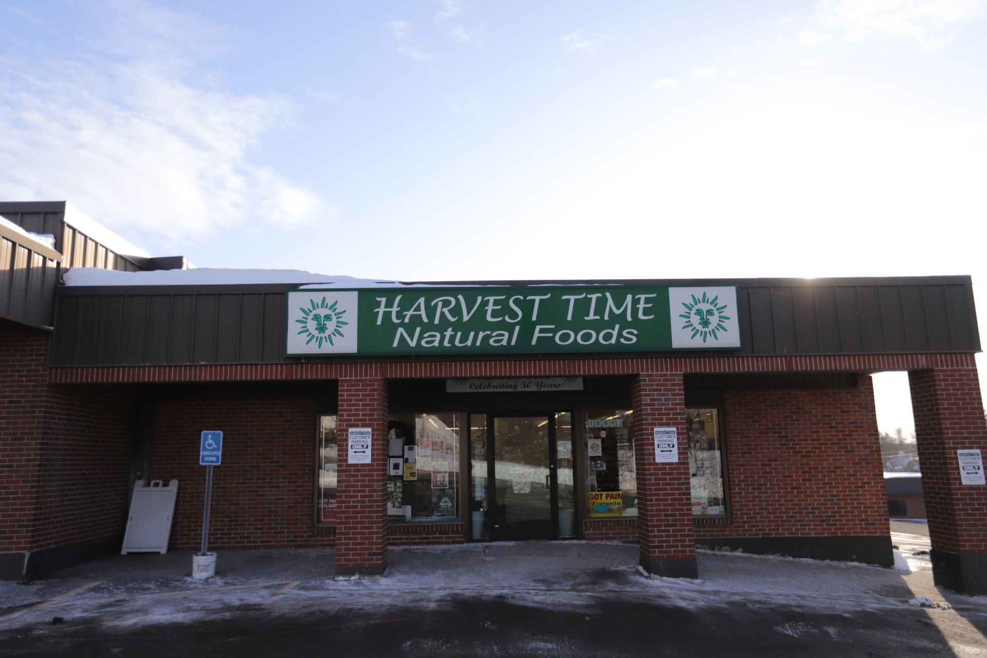 Storefront of Harvest Time Natural Foods, featuring a green sign on a brick exterior under a blue sky.